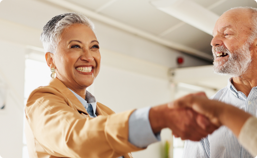 une femme avec un grand sourire qui sert la main à quelqu'un, avec un homme souriant à ses côtés