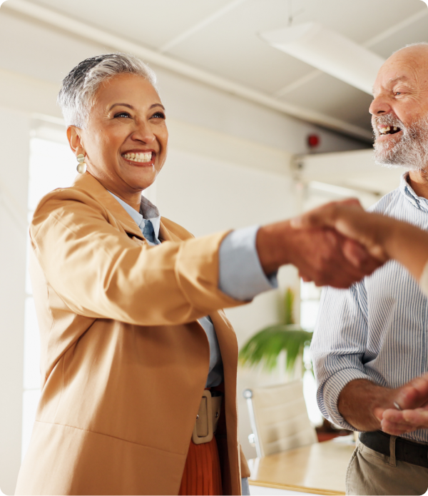 une femme avec un grand sourire qui sert la main à quelqu'un, avec un homme souriant à ses côtés
